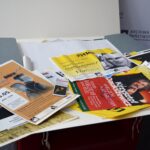Stare plakaty i afisze teatralne wyłożone z dużej, szarej teczki. Na afiszach daty i tytuły wydarzeń organizowanych przez Teatr Propozycji "Dialog" w Koszalinie.