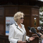 Kobieta w blond włosach i okularach przeciwsłonecznych udziela wywiadu na tle archiwalnego fotoplastikonu w Mielnie.