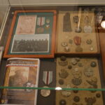 Fragment ekspozycji. W gablocie ułożone stare pamiątki wojenne: zdjęcia, medale i resztki nieśmiertelników.
