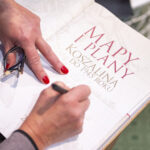 Kobieta podpisuje książkę pt. Mapy i plany Koszalina do 1945 roku. W kadrze widać jedynie stronę tytułową książki i dłonie kobiety.