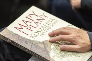 Okładka książki Mapy i plany Koszalina do 1945 roku. Na książce dłoń.