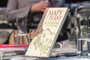 Książka Mapy i plany Koszalina do 1945 roku stoi na stojaku na stole. W ten sposób została wyeksponowana.