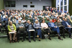 Publiczność w sali kinowej. Ludzie trzymają na kolanach książkę.