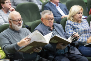 Dwaj starsi mężczyźni siedzą na fotelach i przeglądają publikację.
