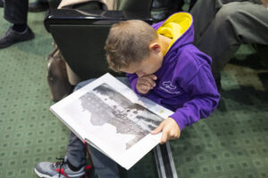 Chłopiec w fioletowej bluzie siedzi na schodkach i przegląda publikację.
