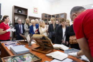Kilkanaście osób zebranych w niewielkim pomieszczeniu. Oglądają stare księgi, fotografie i gęsie pióra rozłożone na stołach i słuchają kobiety w czerwonej koszulce, która opowiada.
