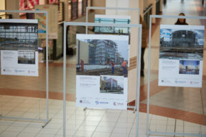 Fragment wystawy w centrum handlowym. Cztery stojaki wystawowe z wyeksponowanymi zdjęciami budynków.