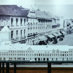 Biała makieta budynków z lat 30. XX wieku na tle starej fotografii ściennej ukazującej te same obiekty.