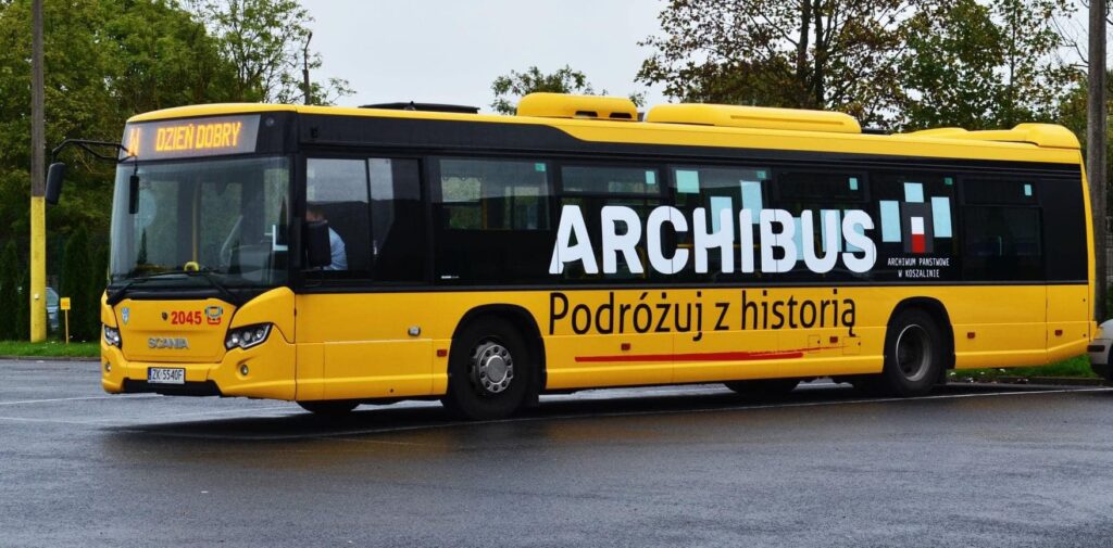 Żółty autobus miejski stoi na parkingu. Na jego boku widnieje napis Archibus Podróżuj z historią.