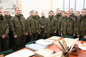 Grupa żołnierzy stoi wokół stołu, na którym leżą materiały archiwalne.