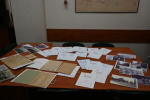 Stare dokumenty, fotografie oraz kroniki pioniera ułożone na dużym stole.