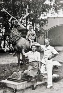 Czarno-białe zdjęcie kobiety i mężczyzny obok pomnika jelenia. Na pomniku siedzi dziecko.