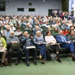 Publiczność w sali kinowej. Ludzie trzymają na kolanach książkę.