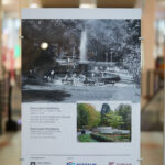 Stojak wystawowy z wyeksponowanym zdjęciem fontanny w parku w przeszłości i dziś.