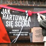 Odwrócona tyłem kobieta w siwych włosach przecina wstęgę znajdującą się na planszy wystawowej o tytule "Jak hartowała się scena". Po lewej stronie stoi druga kobieta w beżowym płaszczu. Przygląda się sytuacji z uśmiechem.